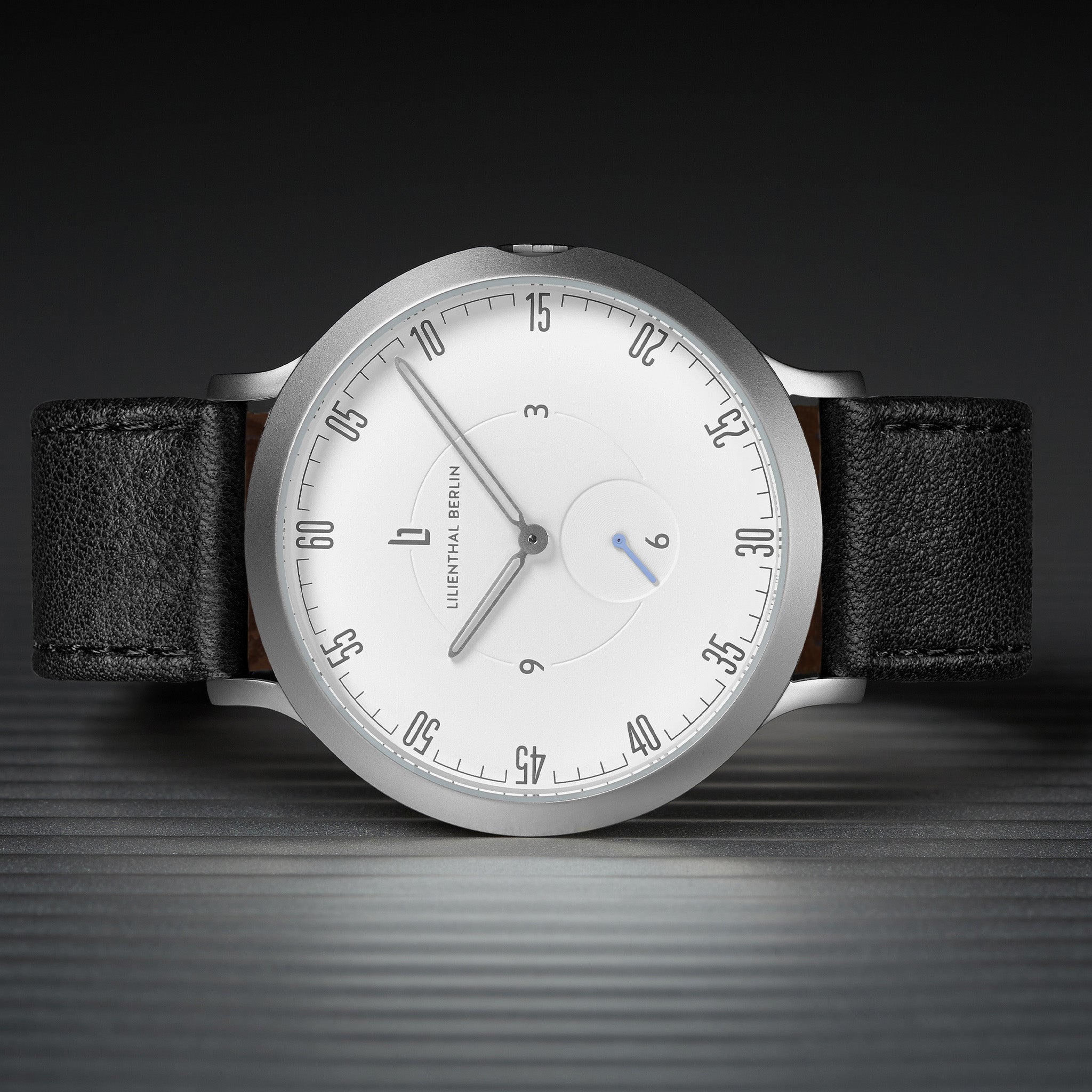 Minimalist silver watch with white dial, black leather strap, and sleek hour markers