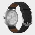 Stainless steel watch case back with black leather strap, visible detailed engravings