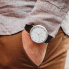 Minimalist silver wristwatch with white dial and black band on wrist, hand in pocket