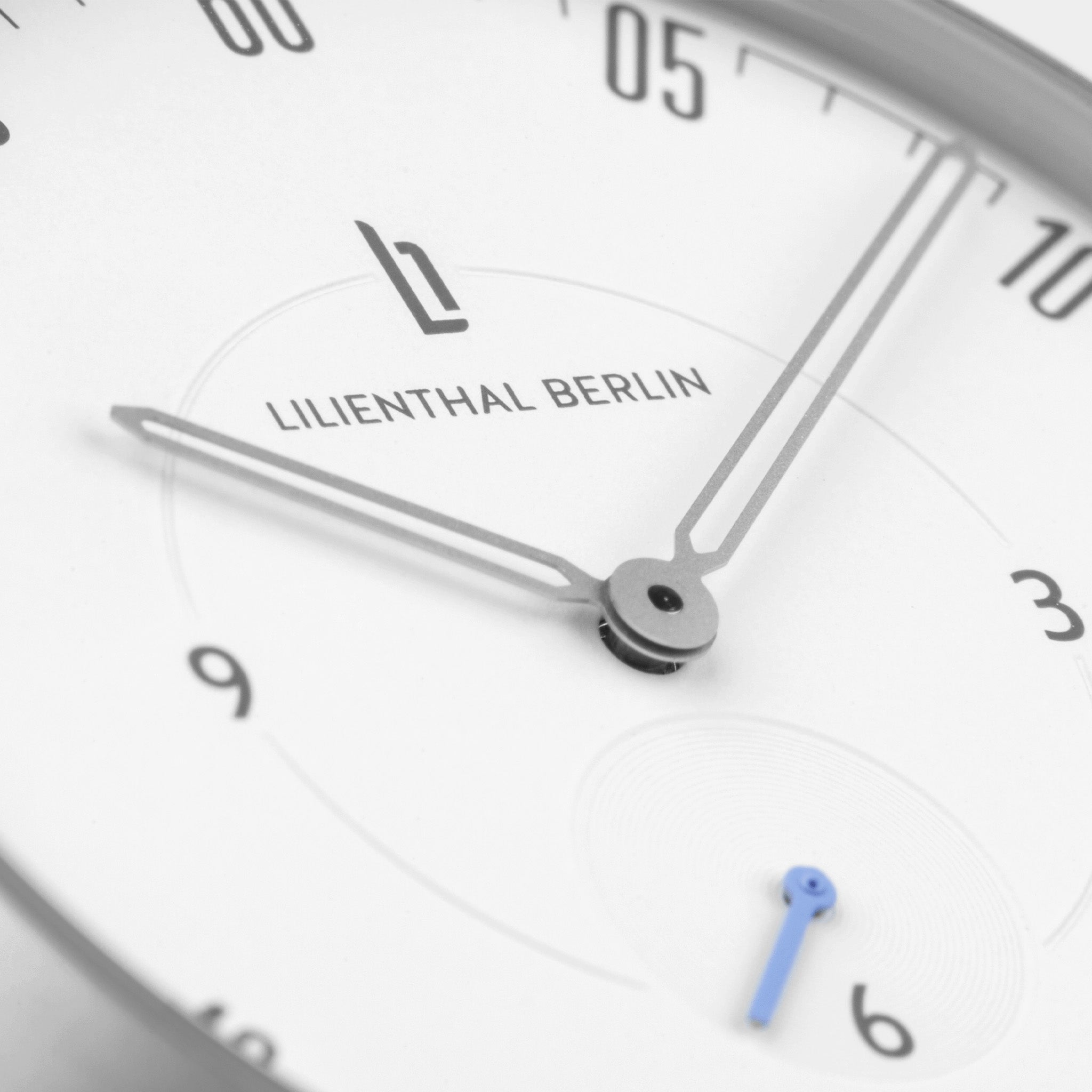 Minimalist wristwatch close-up with silver hands, white dial, and blue subdial hand