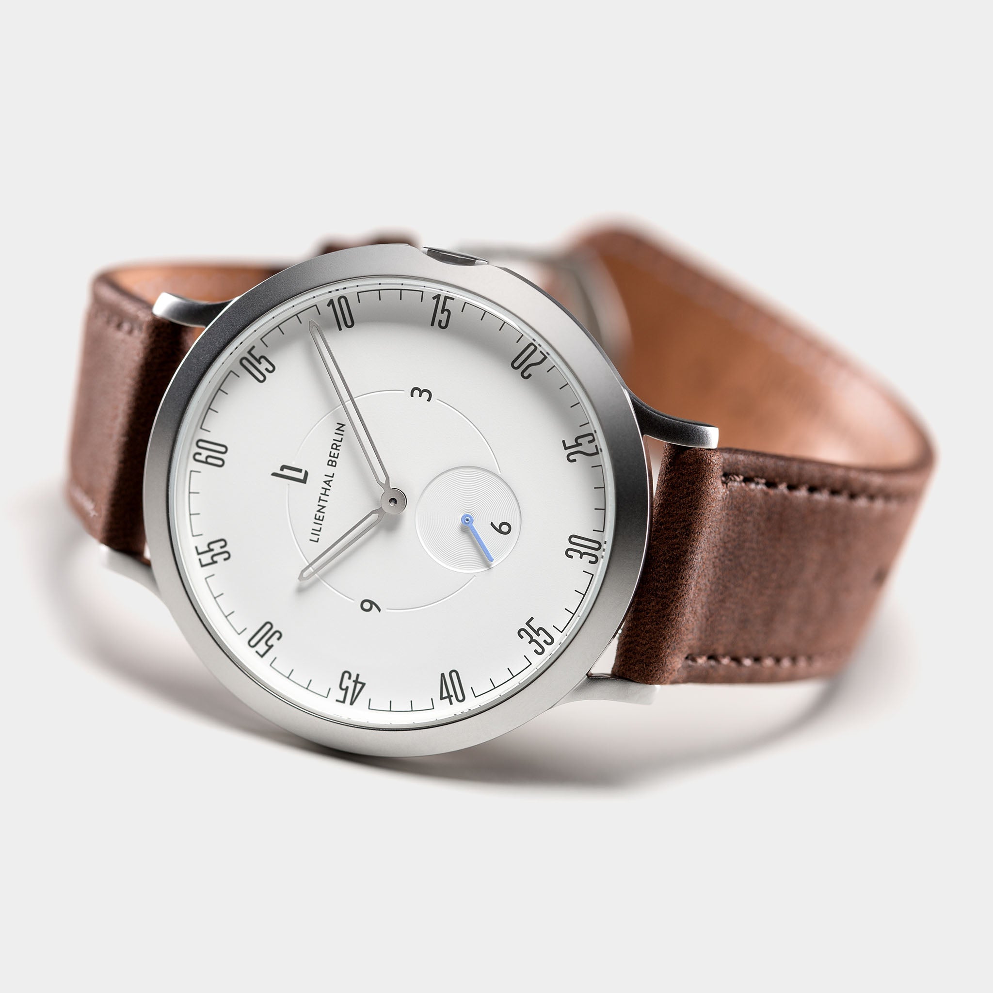 Minimalist silver watch with white dial and brown leather strap on light background
