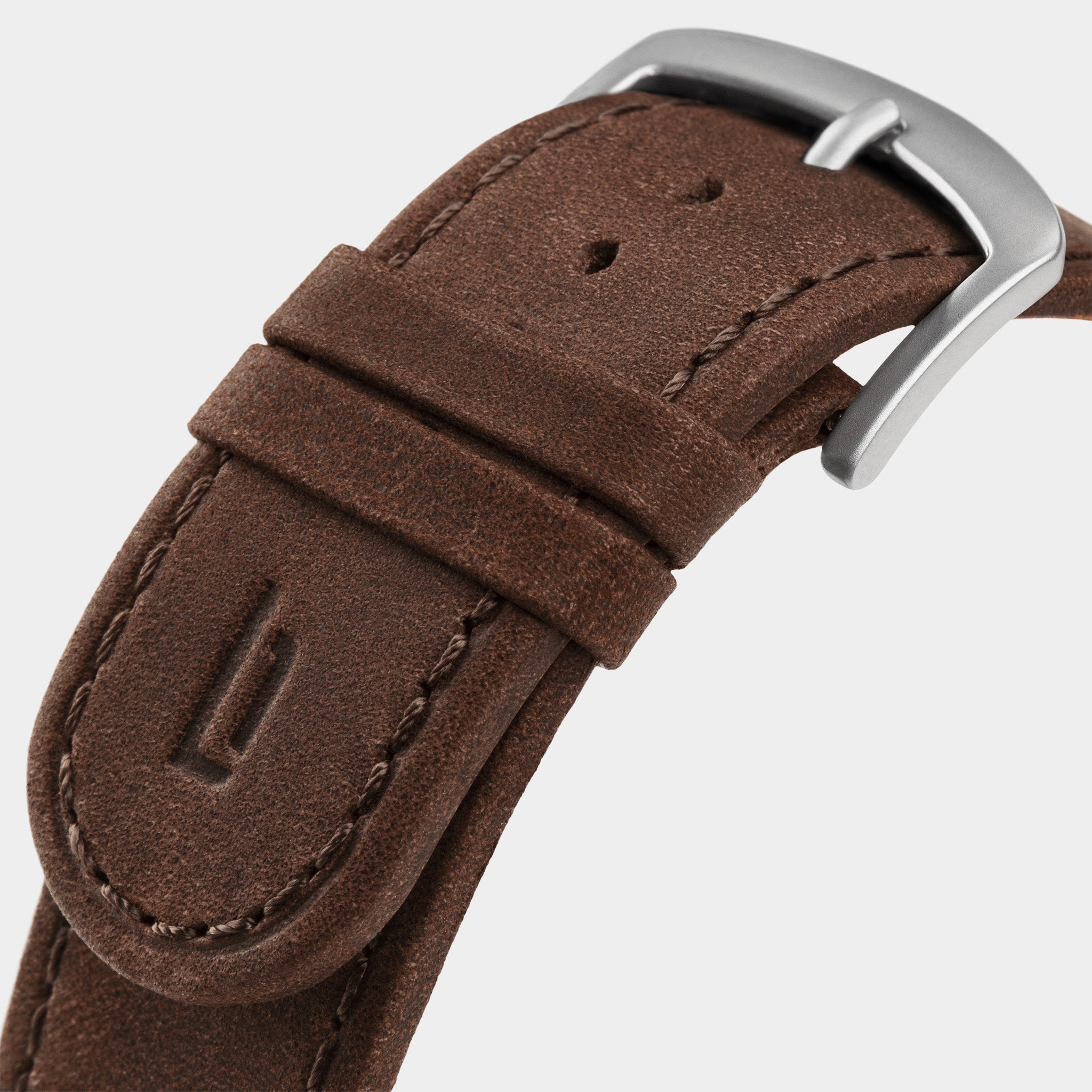 Close-up of a brown leather watch strap with silver buckle and embossed detail