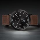 Minimalist black dial watch with brown leather strap on textured surface