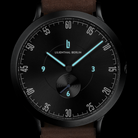 Modern black wristwatch with blue luminous hands, black dial, minimalist design, brown strap