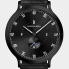 Black minimalist watch with white markers, subdial, and black leather strap on white background