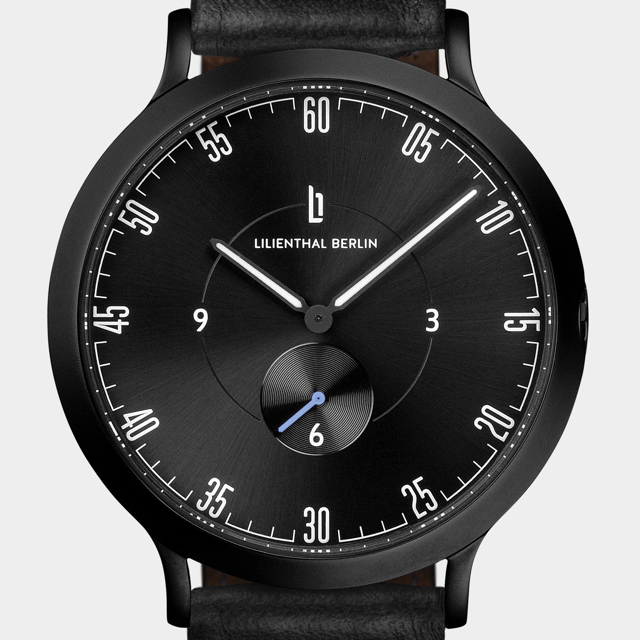 Black minimalist watch with white markers, subdial, and black leather strap on white background