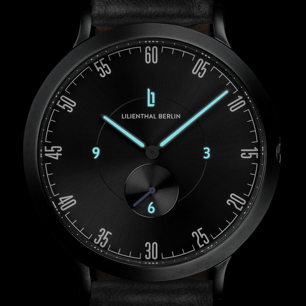 Black minimalist watch with blue luminous hands and leather strap, modern dial design