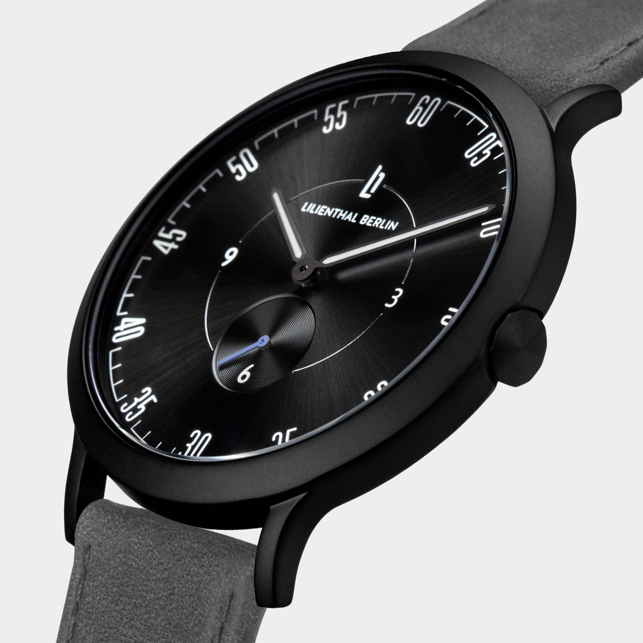 Minimalist black watch with black dial, white markers, and grey suede strap, close-up view.