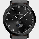 Minimalist black analog watch with white markers, grey strap, subdial, and modern design.