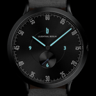 Black minimalist wristwatch with luminous blue hands and a sleek dial, close-up