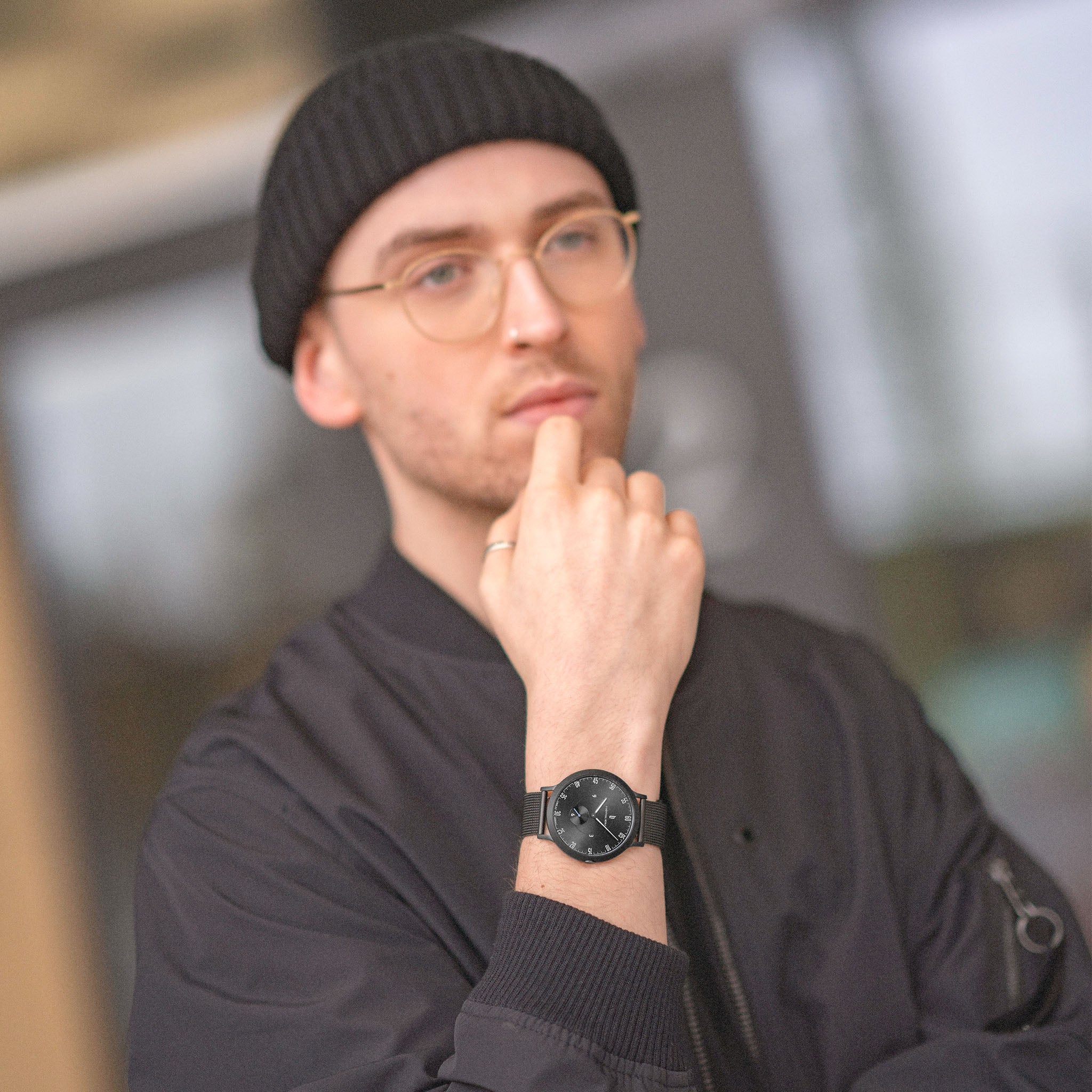 Man wearing black minimalist watch, black beanie, and glasses in urban setting