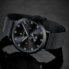 Minimalist black mesh strap wristwatch with black dial on a dark background