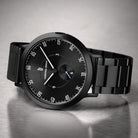 Black minimalist wristwatch with black metal band on a metallic surface