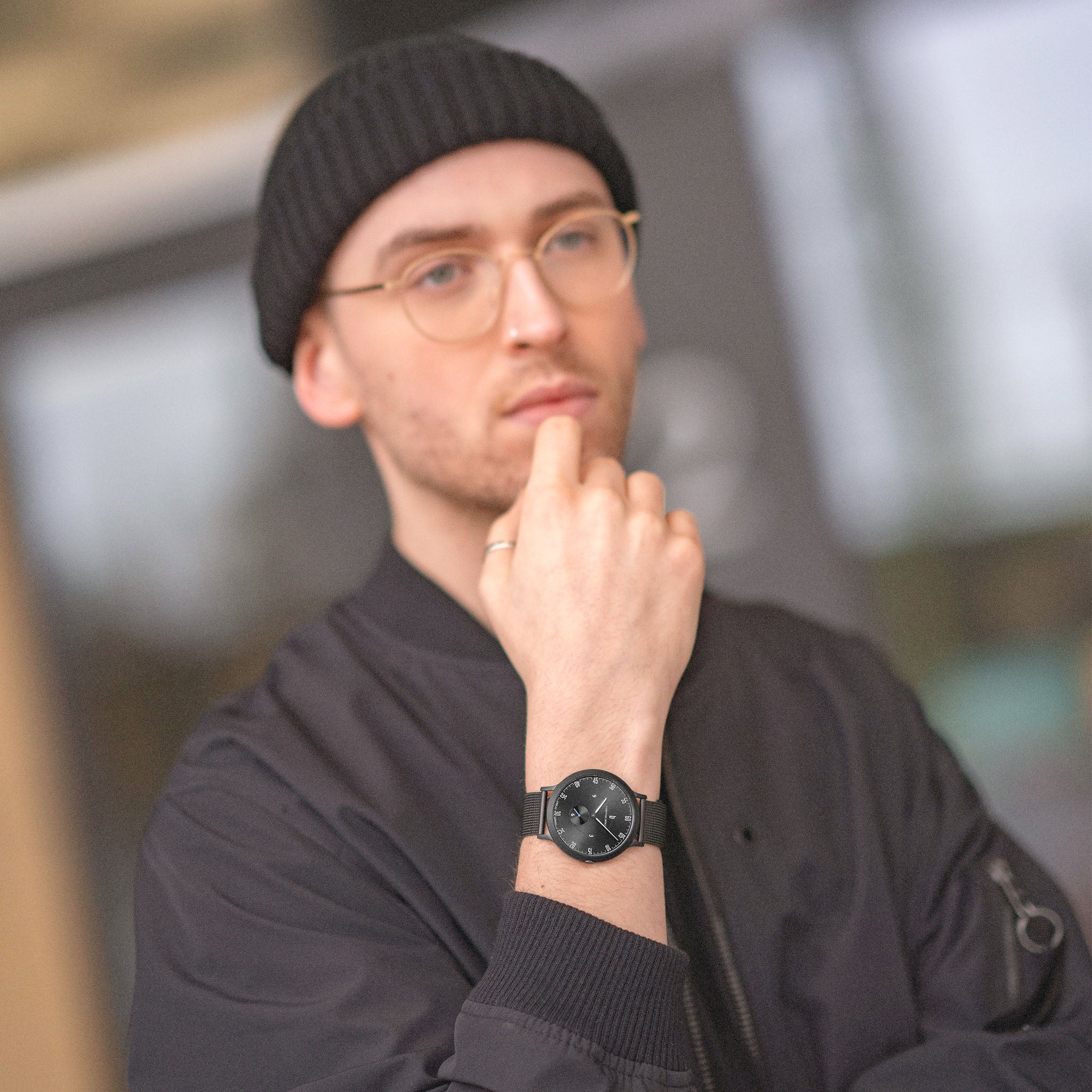Man in black beanie and glasses wearing a modern black wristwatch outdoors
