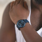 Minimalist black wristwatch with blue leather strap on a person's wrist