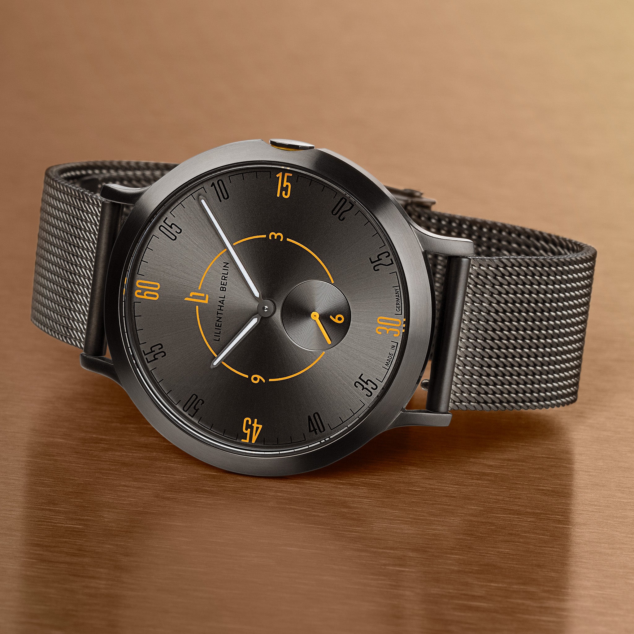 Minimalist black wristwatch with mesh strap, orange accents, and brushed metal dial