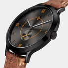 Close-up of a modern black watch with orange details and a textured brown leather strap