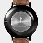 Stainless steel watch case back with engraved details and brown leather strap