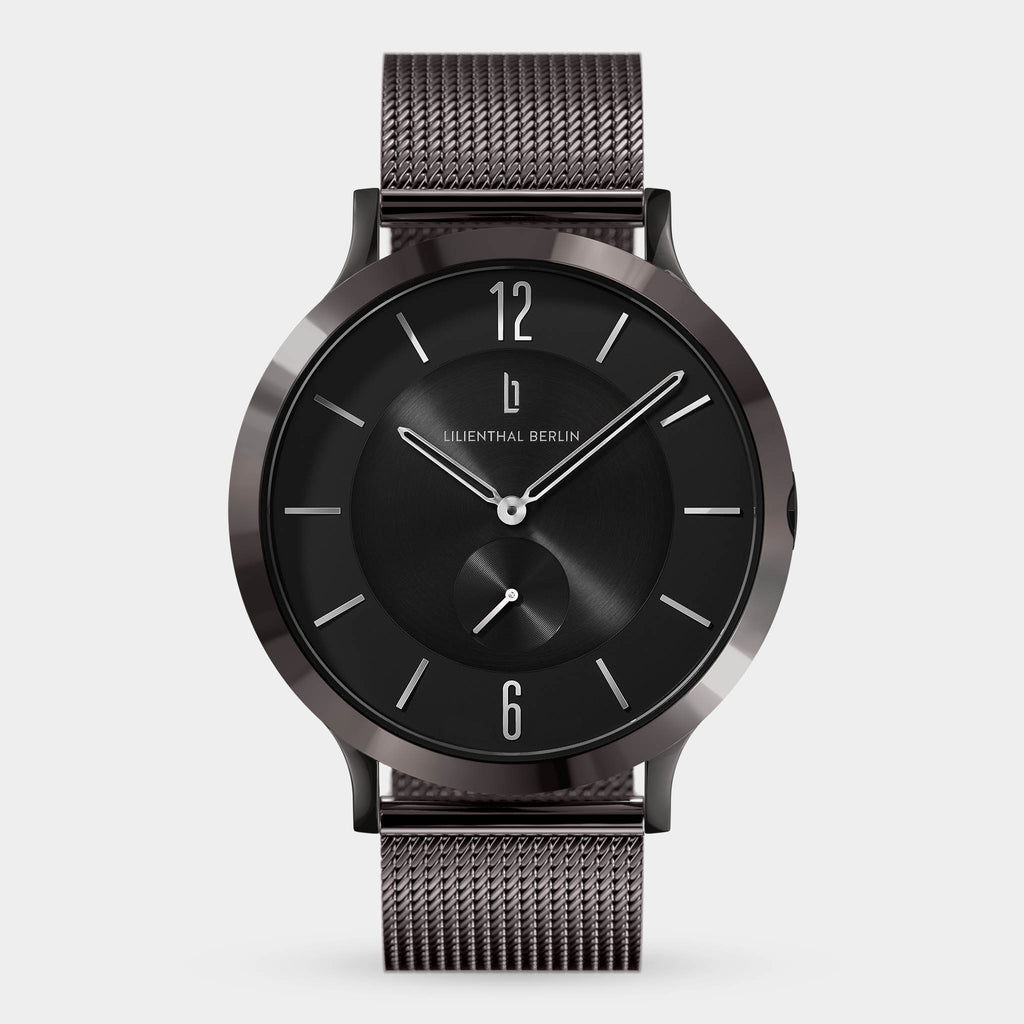 Minimalist black wristwatch with mesh band, round dial, and silver hour markers on white background.
