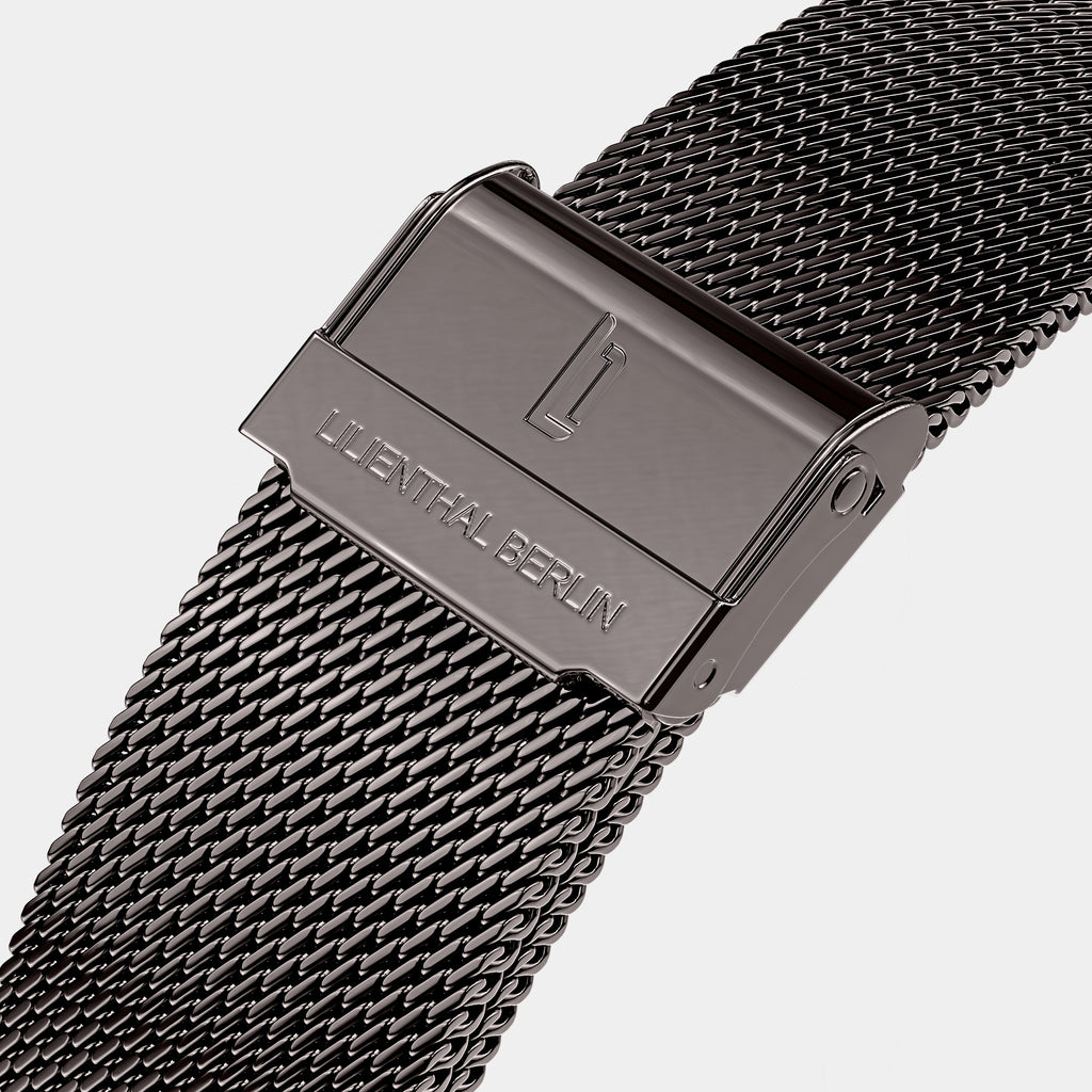 Close-up of a stainless steel mesh watch strap with engraved clasp on white background