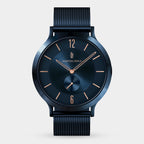 Minimalist blue wristwatch with mesh strap, gold hands, and slim indices on a white background.